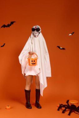 Hayalet kostümü giymiş bir çocuk elinde balkabağı kovasıyla Cadılar Bayramı 'nı neşeyle kutluyor..