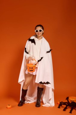 Neşeli bir kız Cadılar Bayramı 'nı neşeli bir kostüm giyerek ve elinde hediye kovası tutarak kutluyor..