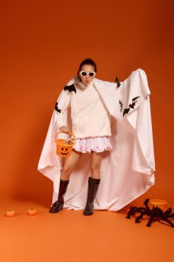 Cadılar Bayramı için giyinmiş bir kız, elinde balkabağı kovası ve şenlikli süslemelerle poz veriyor..