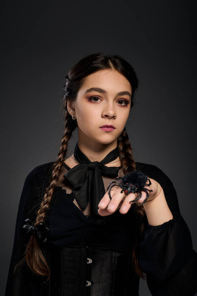 A young girl dressed in a Wednesday costume holds a spider, capturing the Halloween vibe beautifully.