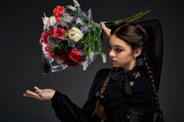 Girl with braids dressed in Wednesday style dress holds a spooky bouquet during Halloween festivities.