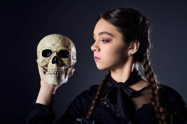Girl with braids in a gothic costume holds a skull while embracing the Halloween spirit.