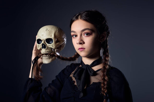 Girl in braided hair wears a gothic dress while holding a skull, Wednesday