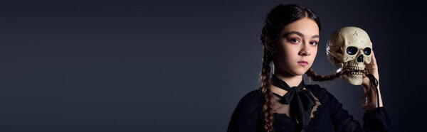 Child dressed in a gothic Wednesday costume holds a skull, capturing Halloween spirit beautifully, banner