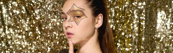 Young girl enjoys Halloween with star face art, surrounded by shiny golden sequins, banner