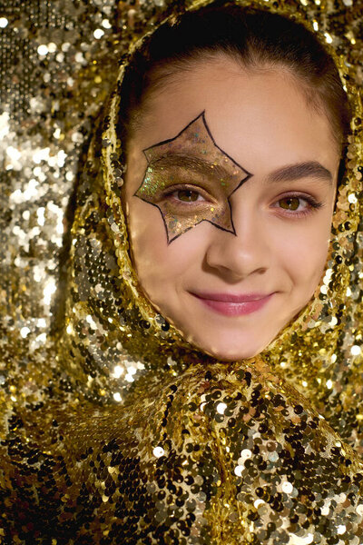 Симпатичная девушка показывает игривую краску на лице звезды в окружении блестящих золотых блёсток.