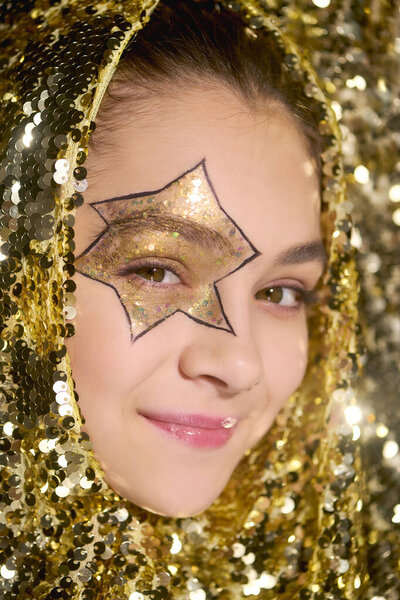 A cheerful girl shows her star face art, surrounded by sparkling golden sequins for Halloween.