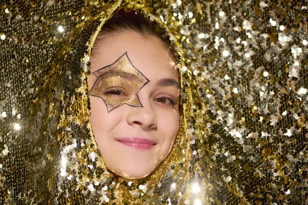 Симпатичная девушка со звездой на лице мерцает в окружении блестящих золотых блесток во время Хэллоуина.