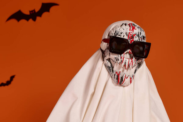 A child celebrates Halloween, wearing a spooky costume against a bright orange background.