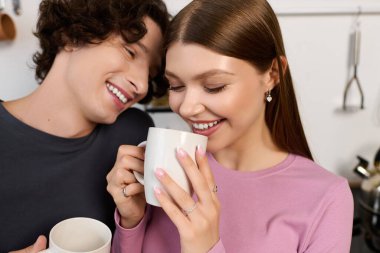 Joyful young couple enjoys hot drinks and love in their stylish apartment kitchen.