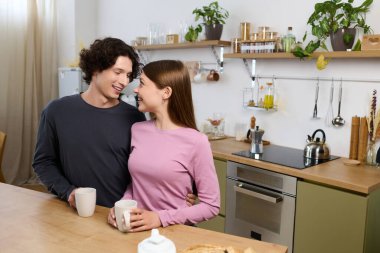 A joyful young couple enjoys each others company in their stylish kitchen while sipping drinks.