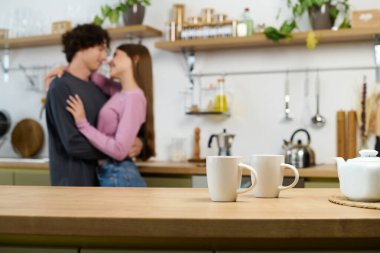 A curly-haired man and beautiful woman share a loving moment in their modern kitchen.