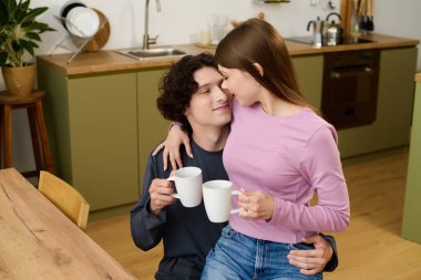 A young couple enjoys each other's company while holding mugs in their stylish kitchen.