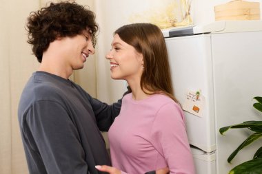 A curly-haired young man and a beautiful woman embrace happily in their modern apartment.