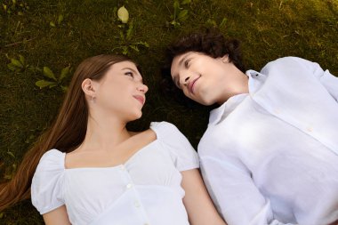 Young couple shares smiles while lying together on soft grass under the warm sun.