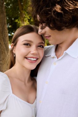 A curly young man and beautiful woman smile at each other, enjoying their time outdoors.