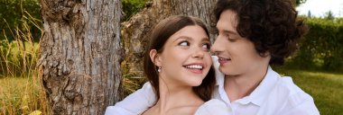 A cheerful young couple relaxes together, smiling and sharing a moment of joy in nature, banner