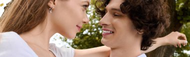 A joyful young couple share a special moment outdoors, smiling at each other under the sun, banner