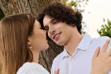 Curly-haired man and beautiful woman share a tender moment outdoors, radiating happiness.