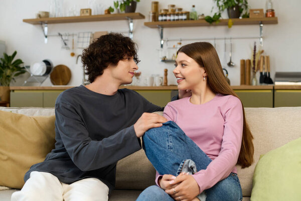 A happy couple sits closely on the couch, enjoying each others company in their cozy home.