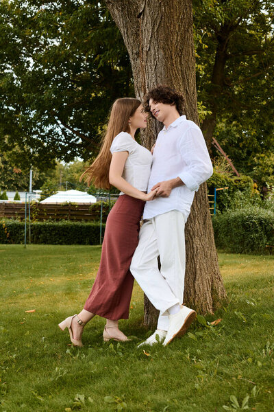 A happy couple shares a loving moment outdoors by a tree, embracing joy and youth.