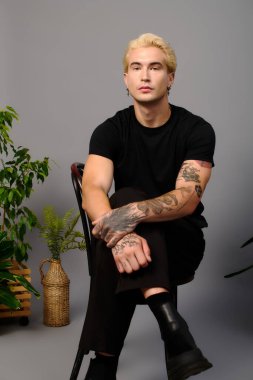 Şık bir genç güvenli bir şekilde bitkilerle dolu bir yerde oturur..