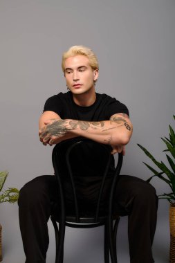 Modaya uygun bir genç, benzersiz stili ve dövmeleri ile çağdaş bir mekanda poz veriyor..