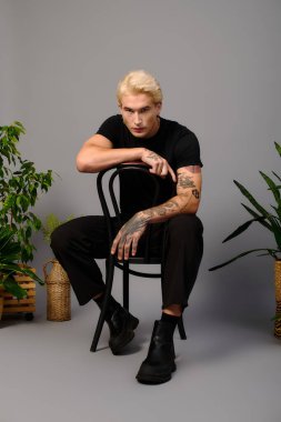 Dövmeli genç adam bitkilerle dolu minimalist bir stüdyoda tarzını sergiliyor..