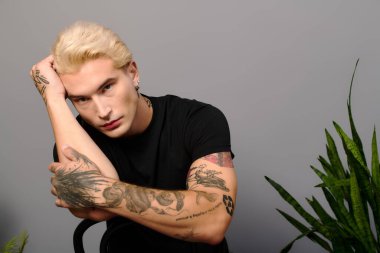 Yakışıklı bir genç, dövmeleri ve büyüleyici bir ifadeyle şık görünümünü sergiliyor..