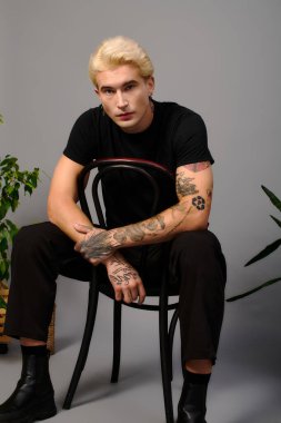 Şık bir genç minimalist bir arkaplana karşı bir sandalyede oturur..