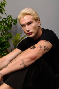 Genç yakışıklı adam, modern gençlik kültürü ve tarzını ifade eden yeşilliğin ortasında düşünceli bir şekilde poz veriyor..