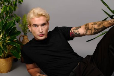 Yakışıklı genç, kendine güvenen bir duruş sergiliyor. Etrafı canlı bitkilerle çevrili..