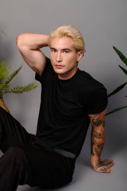 Genç ve çekici bir adam, sakin bir iç mekanda dövmelerini ve son moda saç stilini sergiliyor..