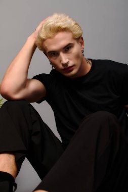 Şık bir genç adam modern bir ortamda rahatça oturur ve rahat bir tutum sergiler..