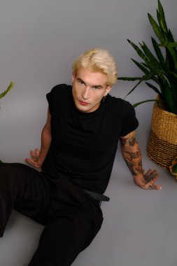 Siyah giyinmiş kendine güvenen bir genç gelişigüzel oturuyor, yeşilliğin ortasında çekici bir tarz sergiliyor..