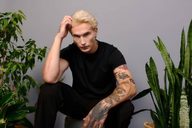 Düşünceli bir genç şık dekorlar ve kapalı mekan bitkilerinin arasında oturur..