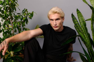 Çekici özellikleri olan yakışıklı bir genç canlı yeşil bitkilerin arasında oturuyor, gençlik kültürünü somutlaştırıyor..