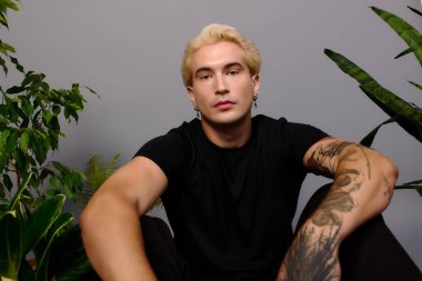 Sarı saçlı şık bir ergen, gençlik modasını ön plana çıkaran gür bitkiler arasında poz veriyor..