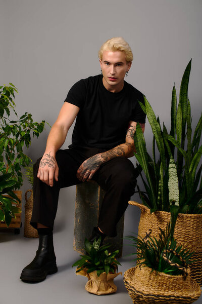 A handsome teenager poses confidently among lush plants in a modern space.