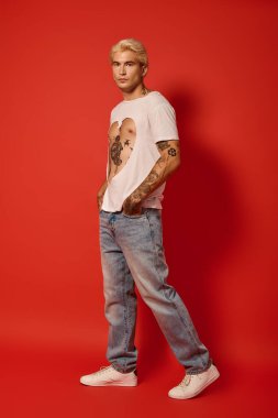 Yakışıklı genç, kendine güvenen bir şekilde poz verirken çarpıcı bir kırmızı arkaplan karşısında moda sergiliyor.