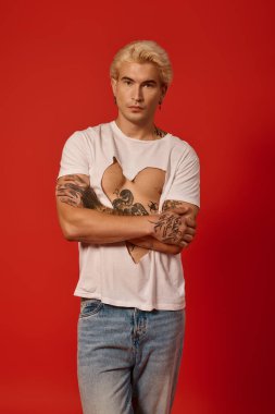 Dövmeli genç adam kendine güvenerek duruyor, genç modasını cesur bir şekilde benimsiyor..