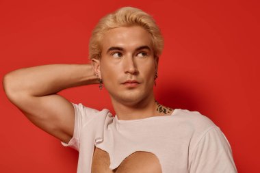 Genç ve yakışıklı bir adam eşsiz bir tişört ve koyu kırmızı arka planla moda anlayışını sergiliyor..