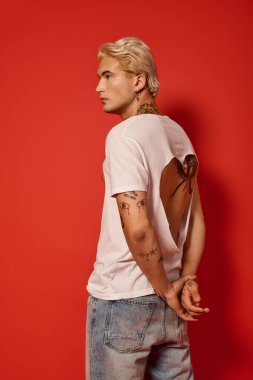 Kendine güvenen bir genç cesur kırmızı bir arka planda duruyor, gençlik kültürü ve tarzı sergiliyor..