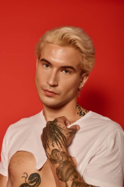 Genç adam moda tarzını ve dövmelerini cesur kırmızı bir zemine karşı sergiliyor..