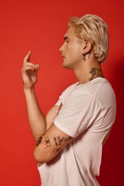 Modayı takip eden bir genç, şık görünüşünü ve dövmelerini sergileyen parlak kırmızı bir duvara karşı duruyor..