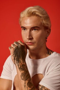 Zarif bir genç, güçlü bir bakışla, dövmelerini ve cazibesini sergileyerek düşünceli bir şekilde poz verir..