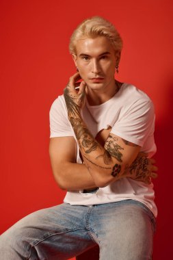 Dövmeleri olan şık bir genç cesur bir kırmızı duvara yaslanır..