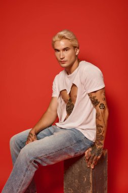 Yakışıklı bir genç, dövmeli kollarını gösterirken ahşap bir blokta poz veriyor..