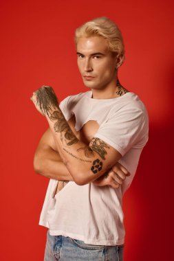 Genç ve çekici bir adam, eşsiz stilini ve özgüvenini cesur bir kırmızı arkaplan önünde sergiliyor..