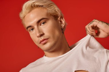 Sarışın ve etkileyici bakışları olan yakışıklı bir genç, çarpıcı bir arka plana karşı özgüvenini gösteriyor..